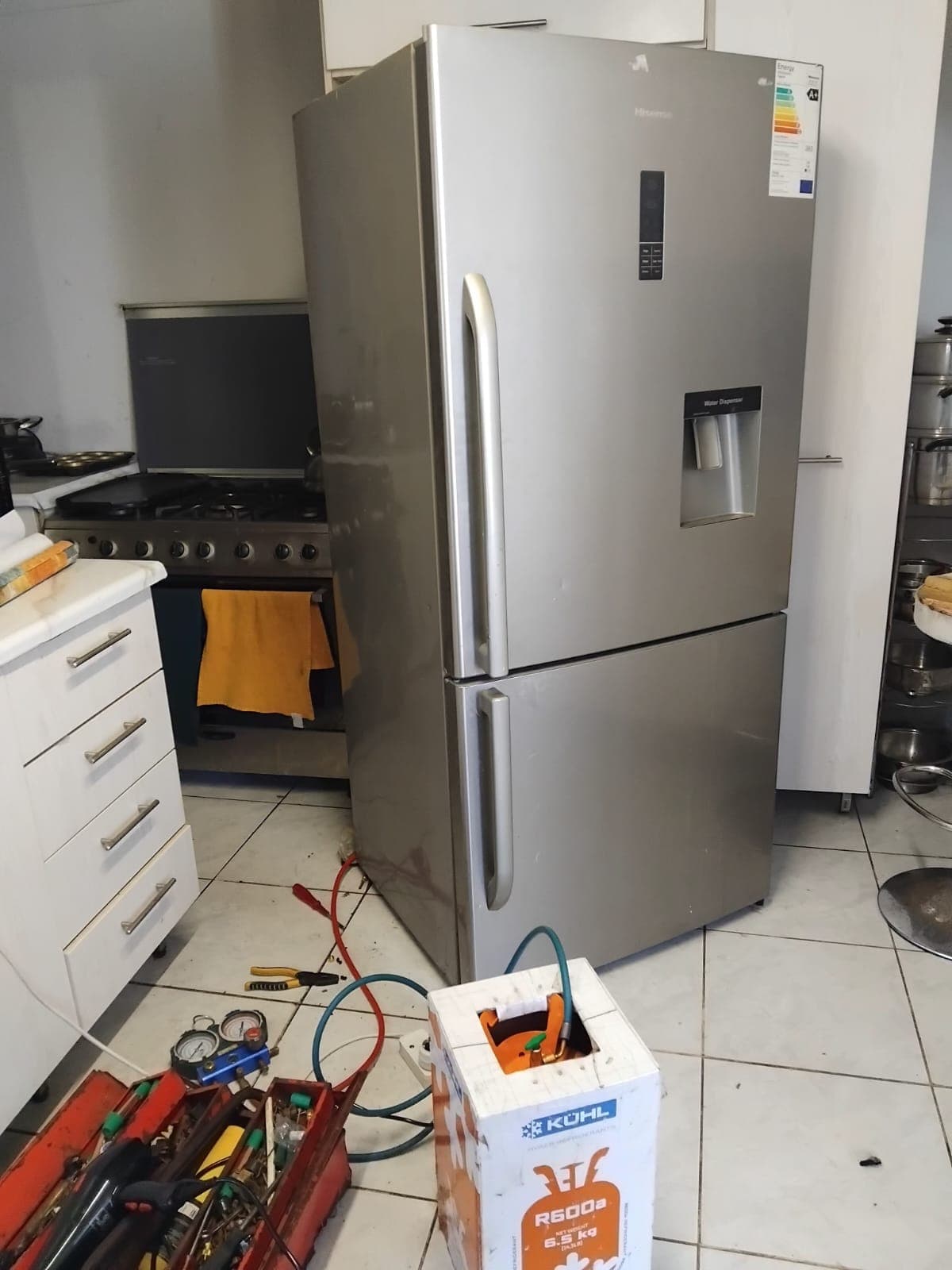 Hisense fridge being regassed on site, with gauges, tools and an R600a cylinder